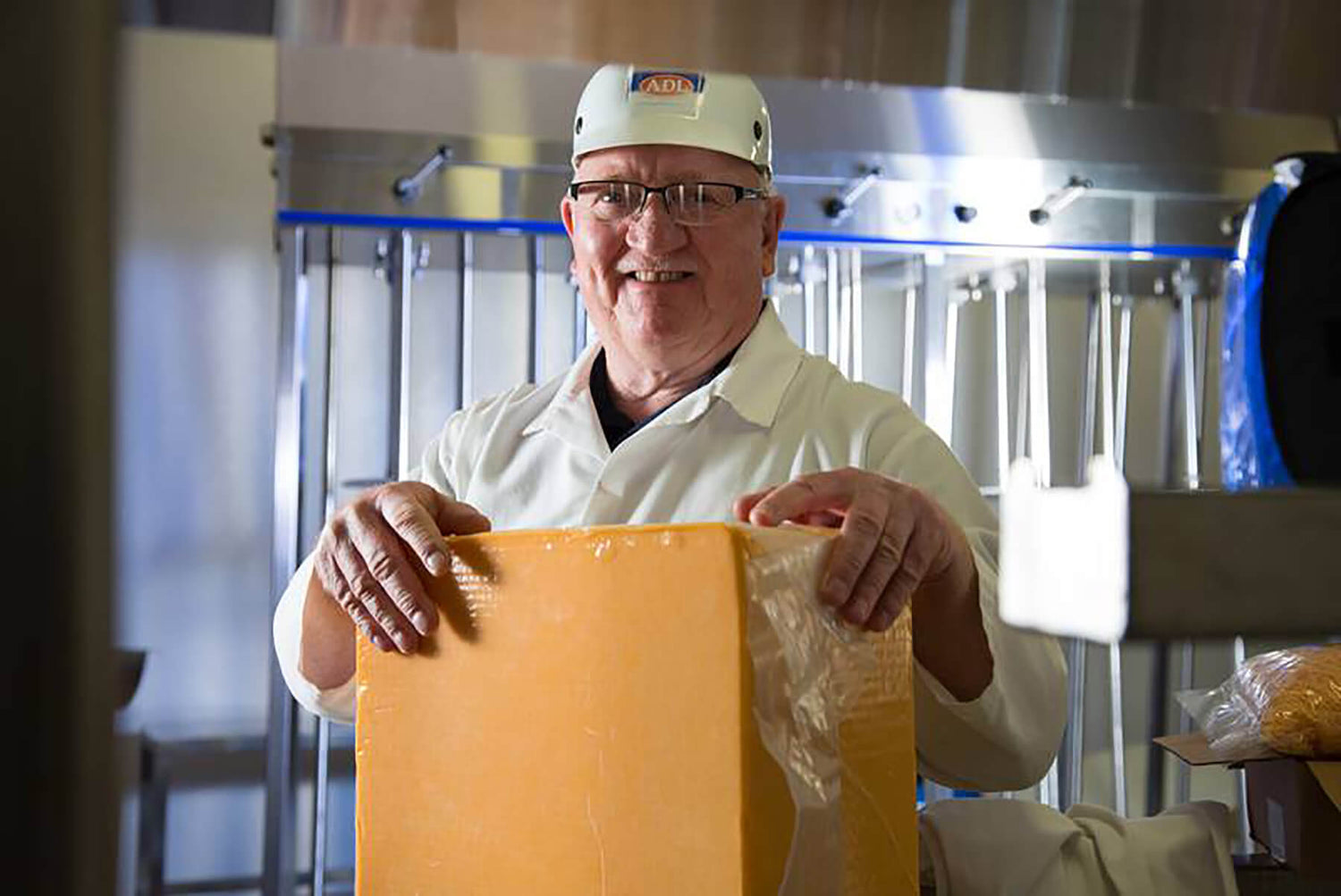 A man stands at the ADL production facility holding a big block of cheddar cheese