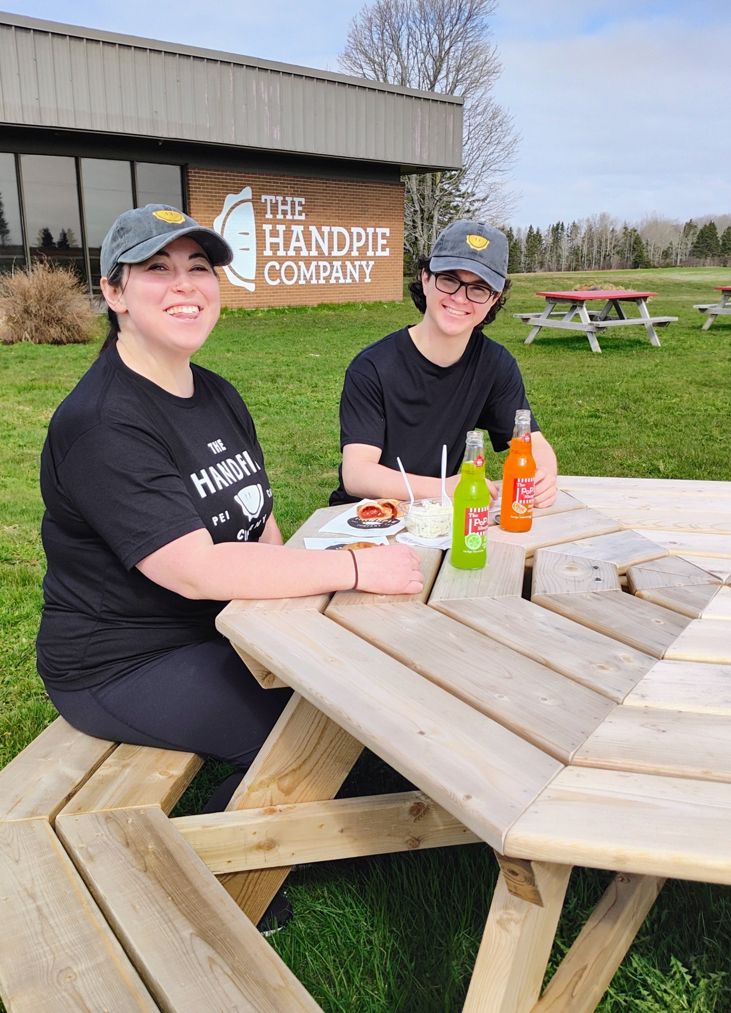 Two Handpie Company Team members enjoy grab-and-go food in PEI at a picnic bench outside HQ in Albany