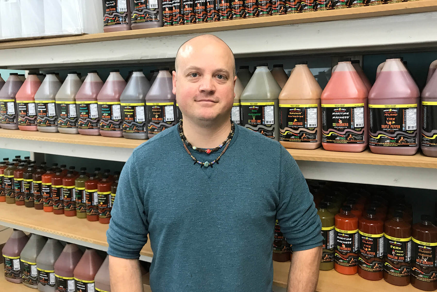 A man standing in front of a wall of hot sauce called Maritime Madness in PEI